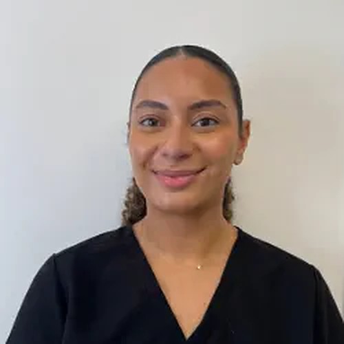 Dr Tia Bahia, dentist, smiling in black scrubs